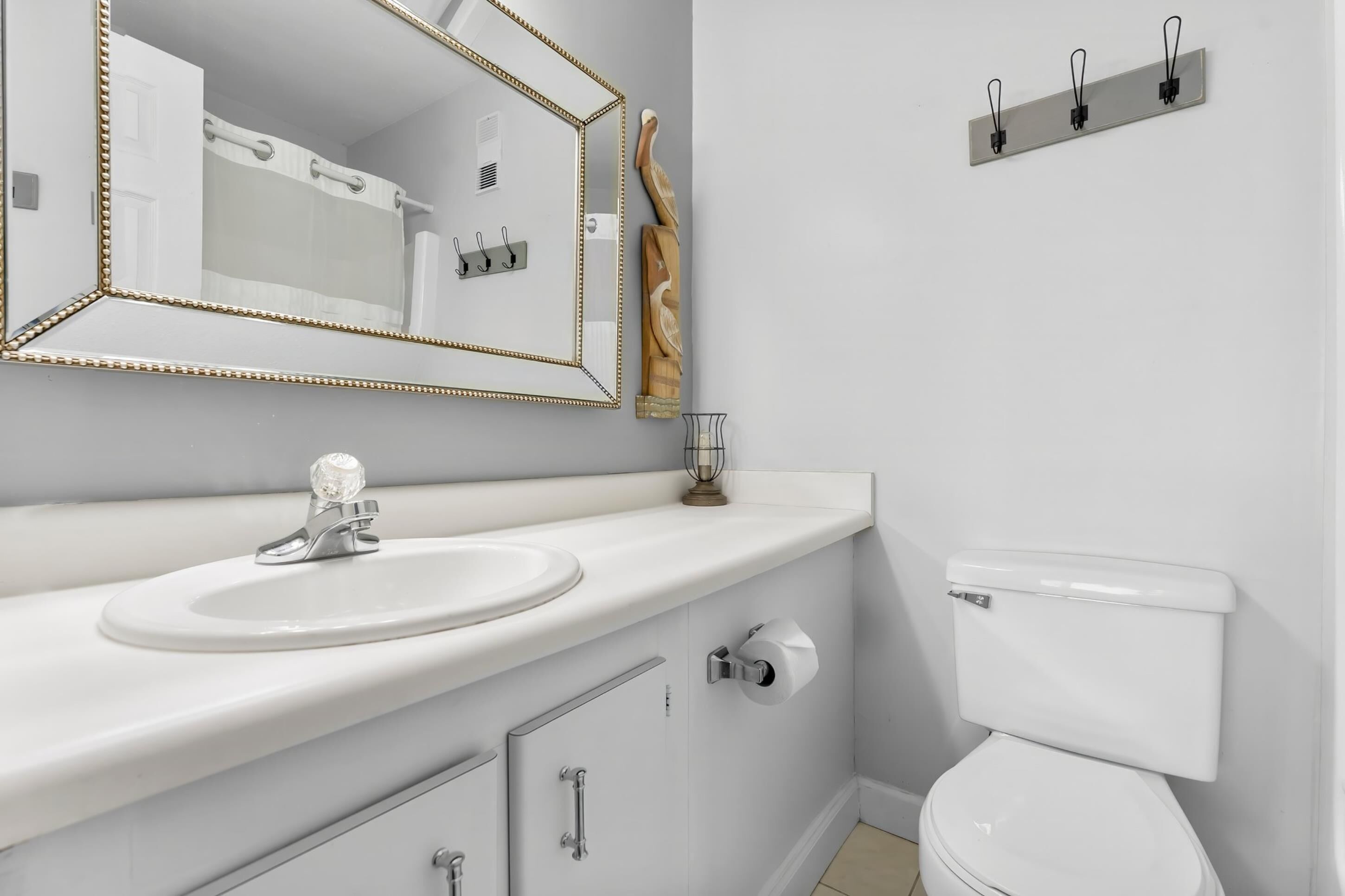 A bathroom with a white sink, a mirror with a gold frame, a toilet, and a towel rack.