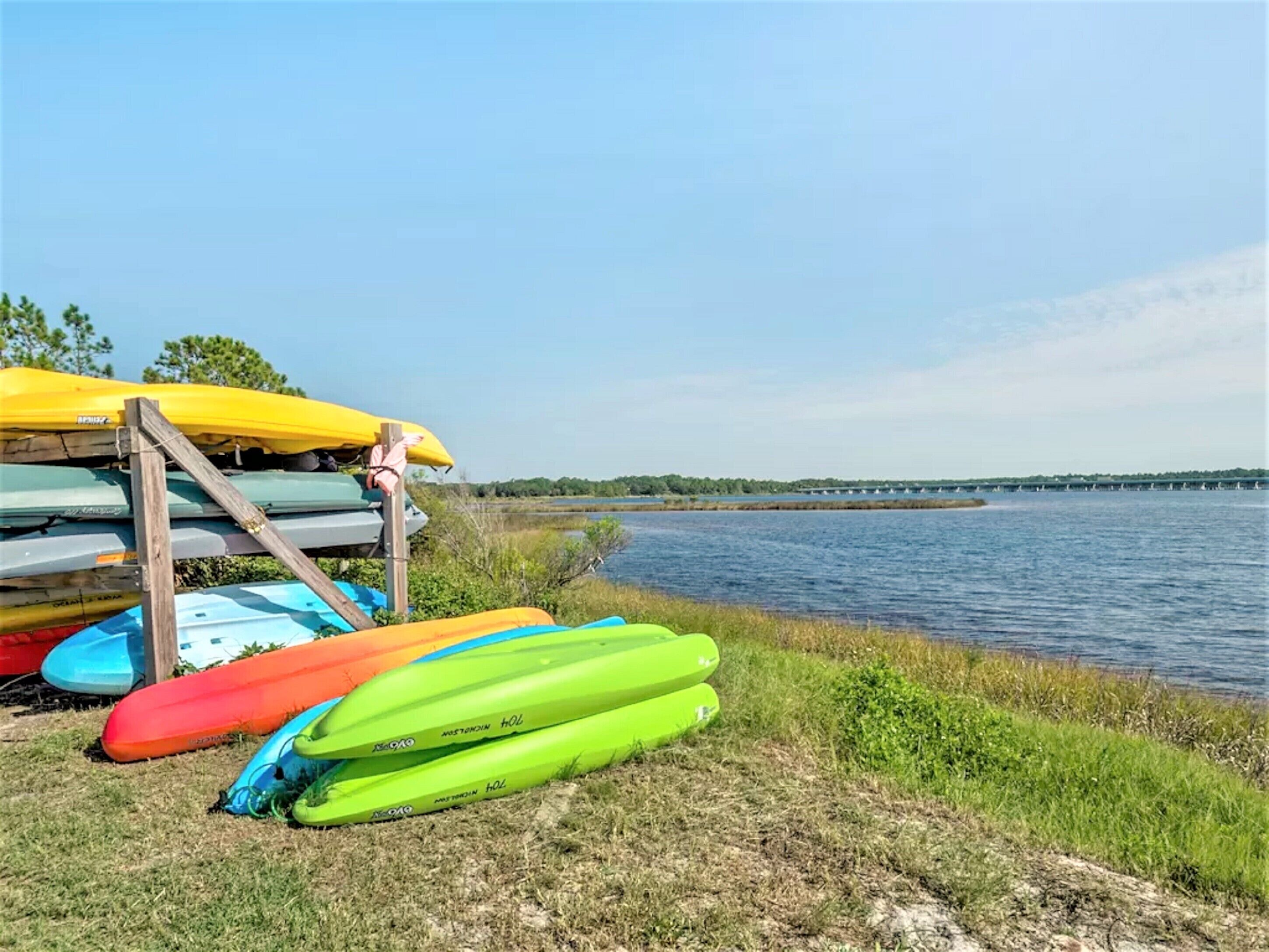 A row of kayaks and canoes stacked on a wooden rack by a calm lake.