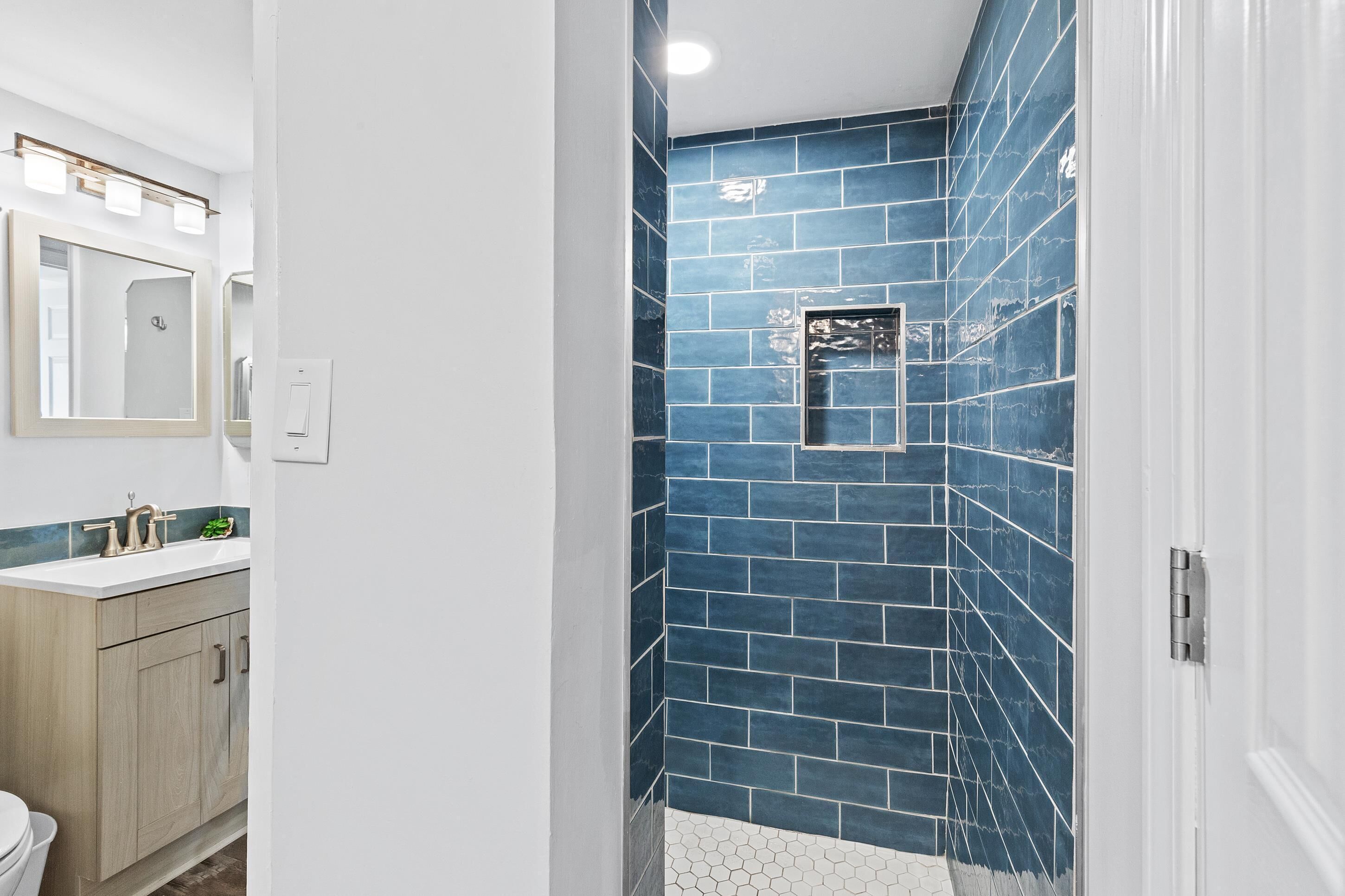 A bathroom with a white sink, wooden cabinets, and a blue-tiled shower area.