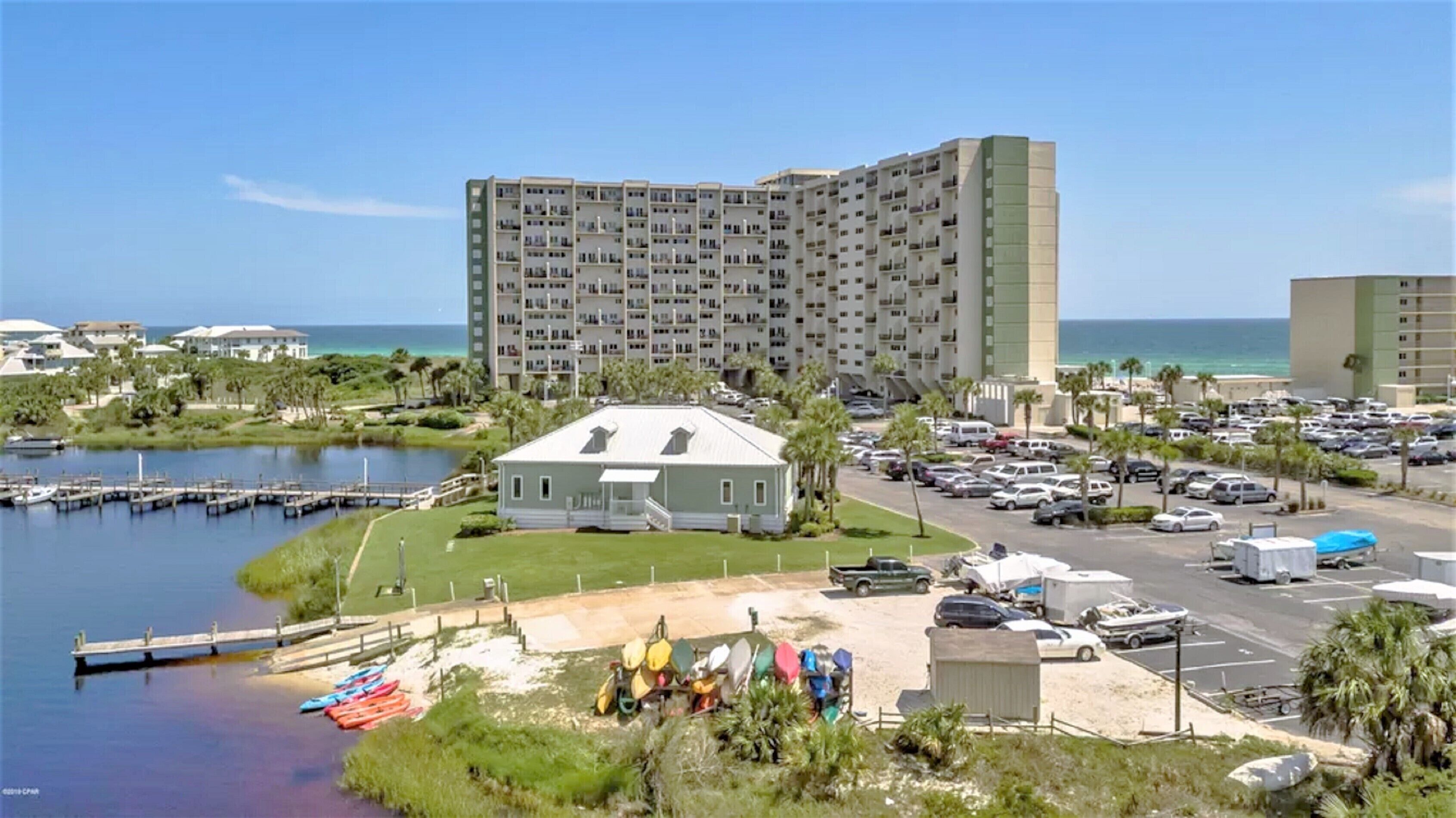 A coastal hotel with multiple floors, a parking lot, and a marina with boats.