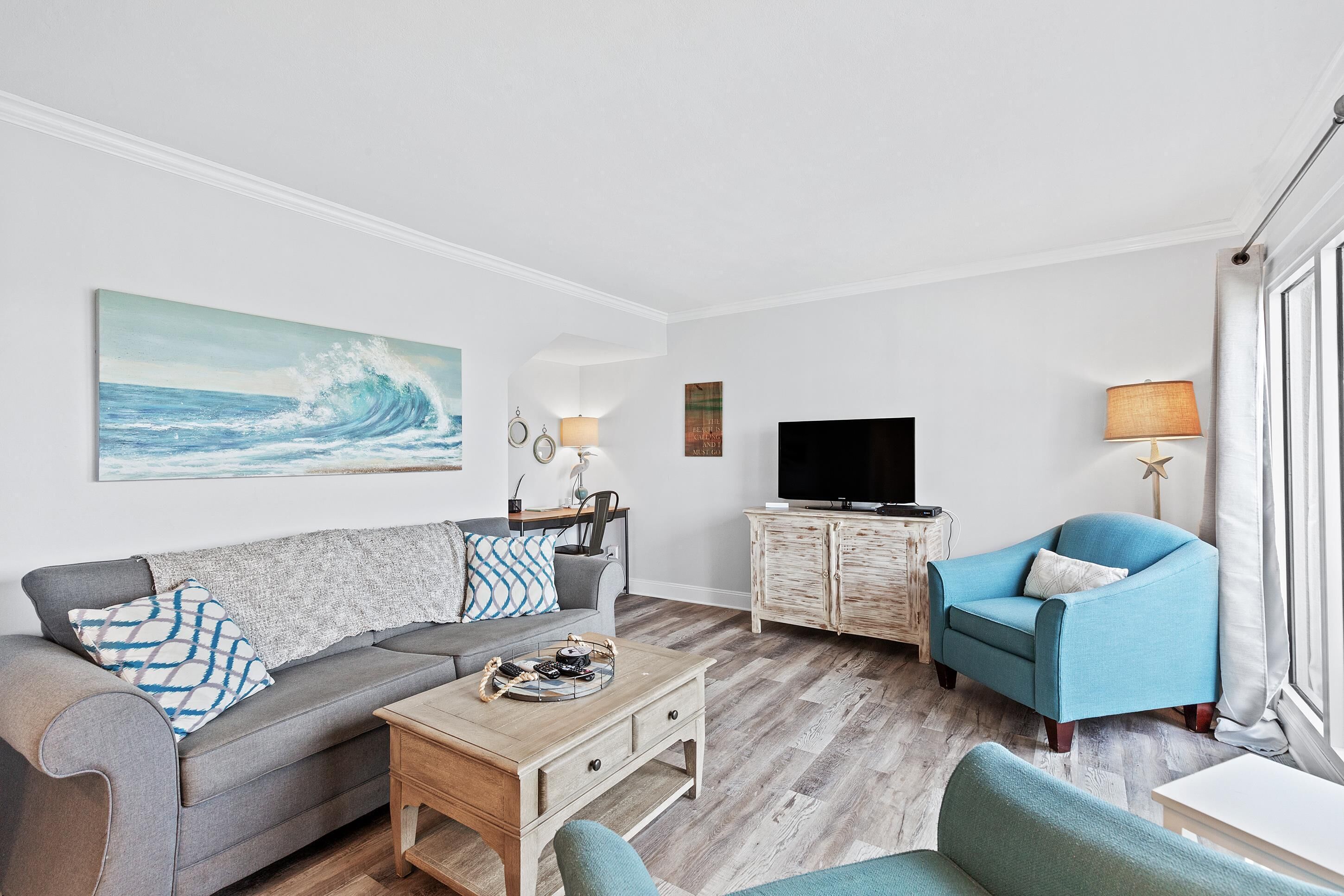 Ein modernes Wohnzimmer mit grauem Sofa, blauem Sessel, Couchtisch aus Holz und Flachbildfernseher.