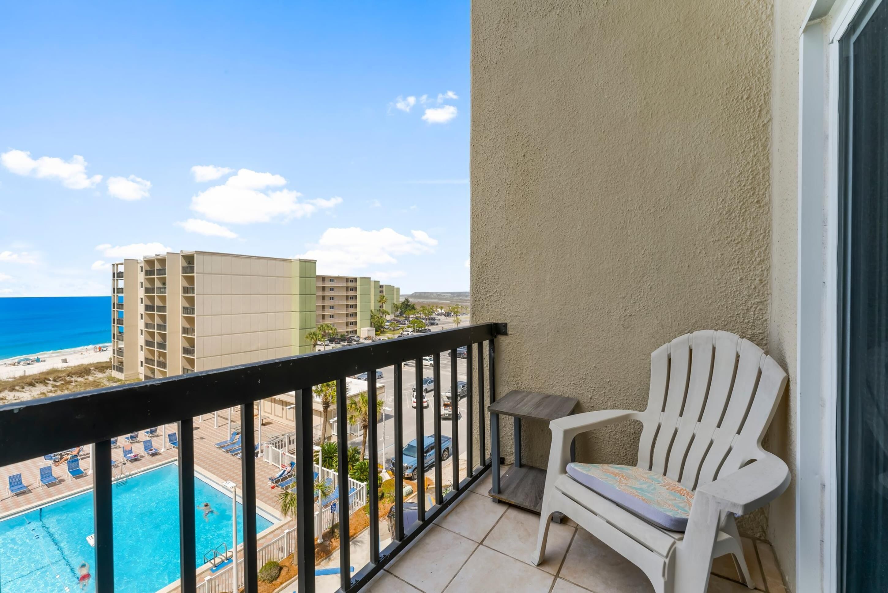 A balcony with a view of a swimming pool, beach, and buildings.