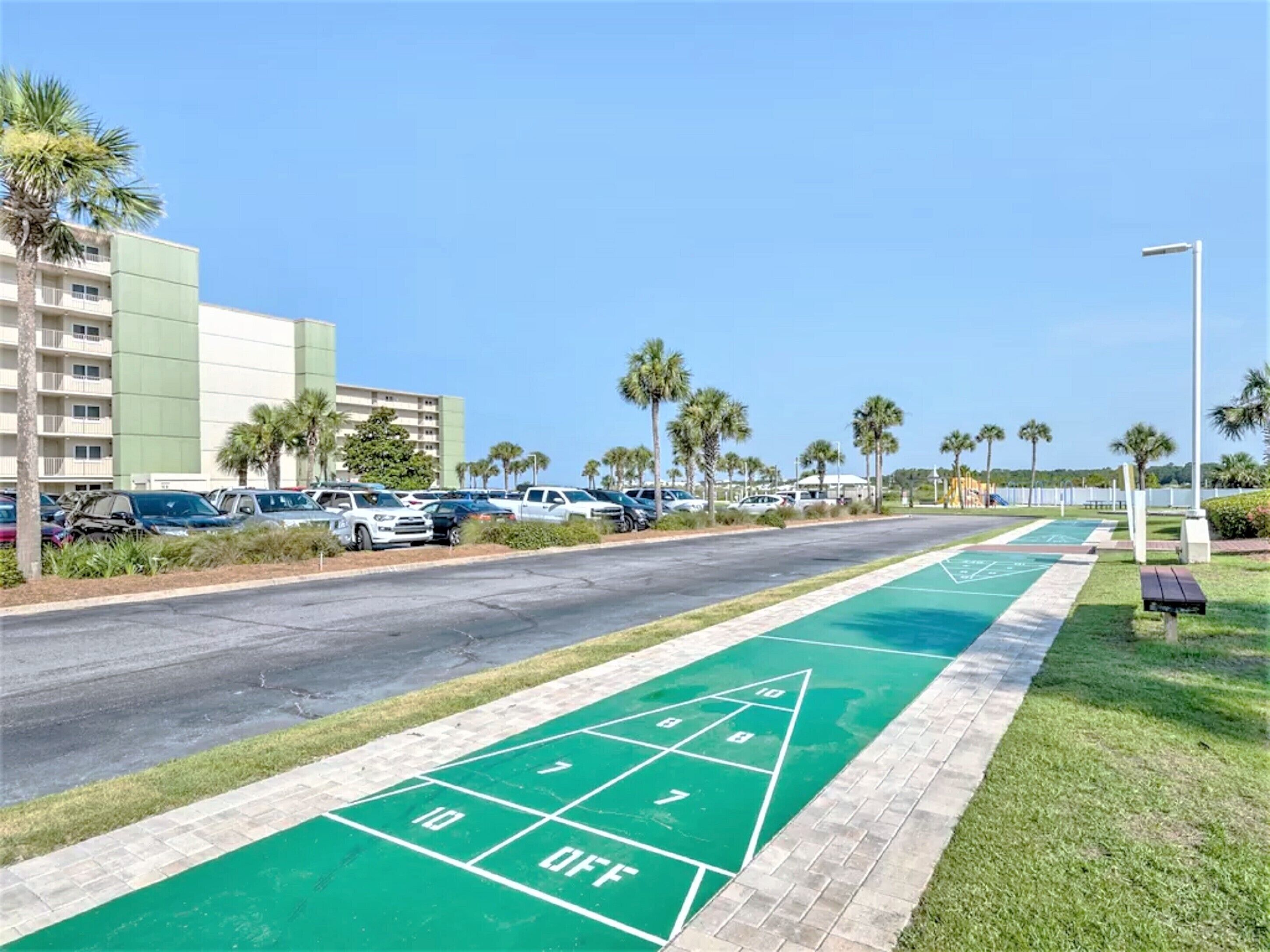 A parking lot with a shuffleboard court, palm trees, and a building in the background.
