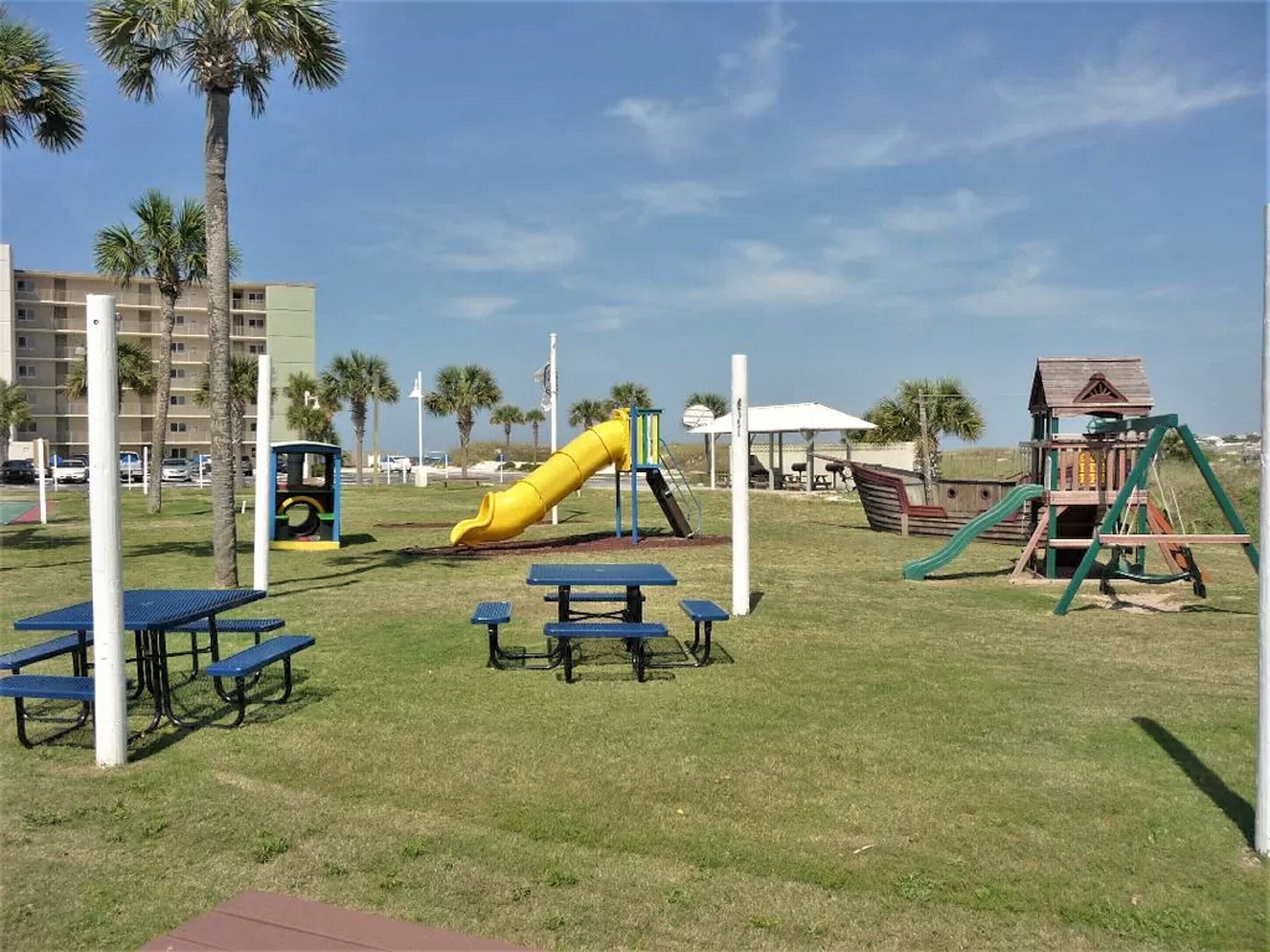 A playground with a yellow slide, picnic tables, and a wooden playhouse.