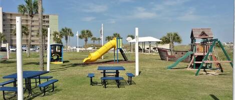 A playground with a yellow slide, picnic tables, and a wooden playhouse.