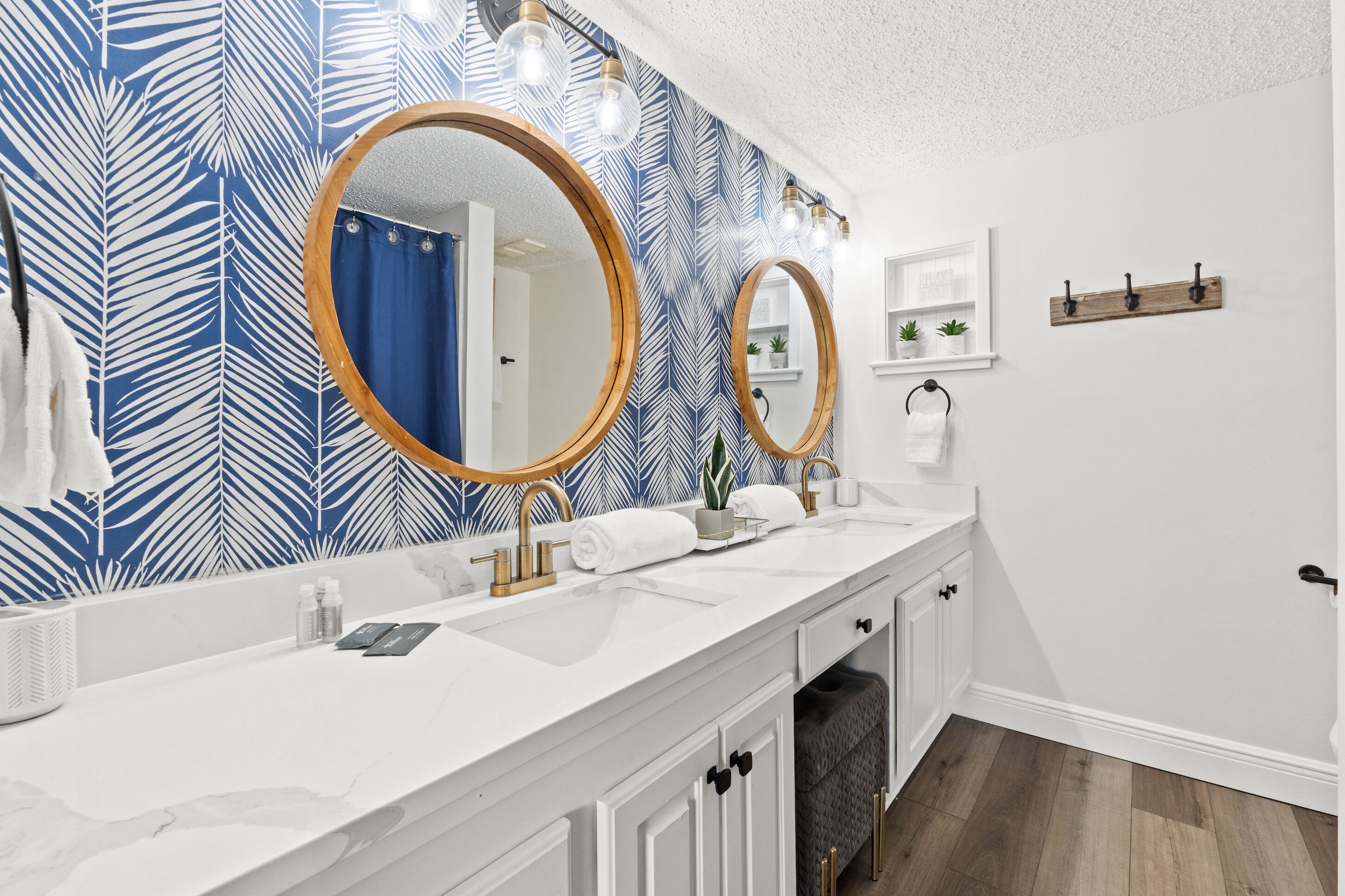 Une salle de bain avec un meuble-lavabo blanc, deux miroirs ronds, un rideau de douche bleu et un mur à motifs.