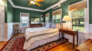 Un dormitorio con una cama grande, una silla de madera, un escritorio y una ventana con vistas al exterior.