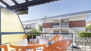A balcony with a round table and orange chairs, potted plants, and a view of a residential building. - Cosy apartment for 4 guests with WIFI, A/C, TV and terrace (Torredembarra)