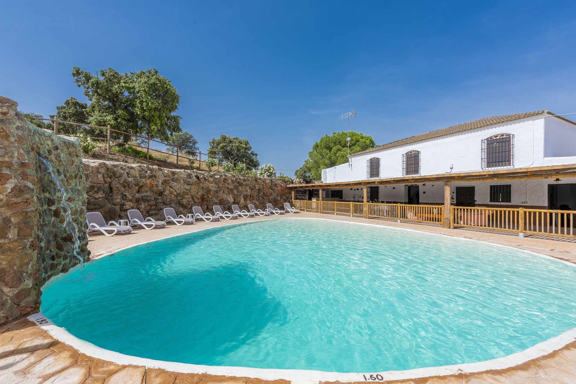 A swimming pool with a stone wall and a white building with windows.