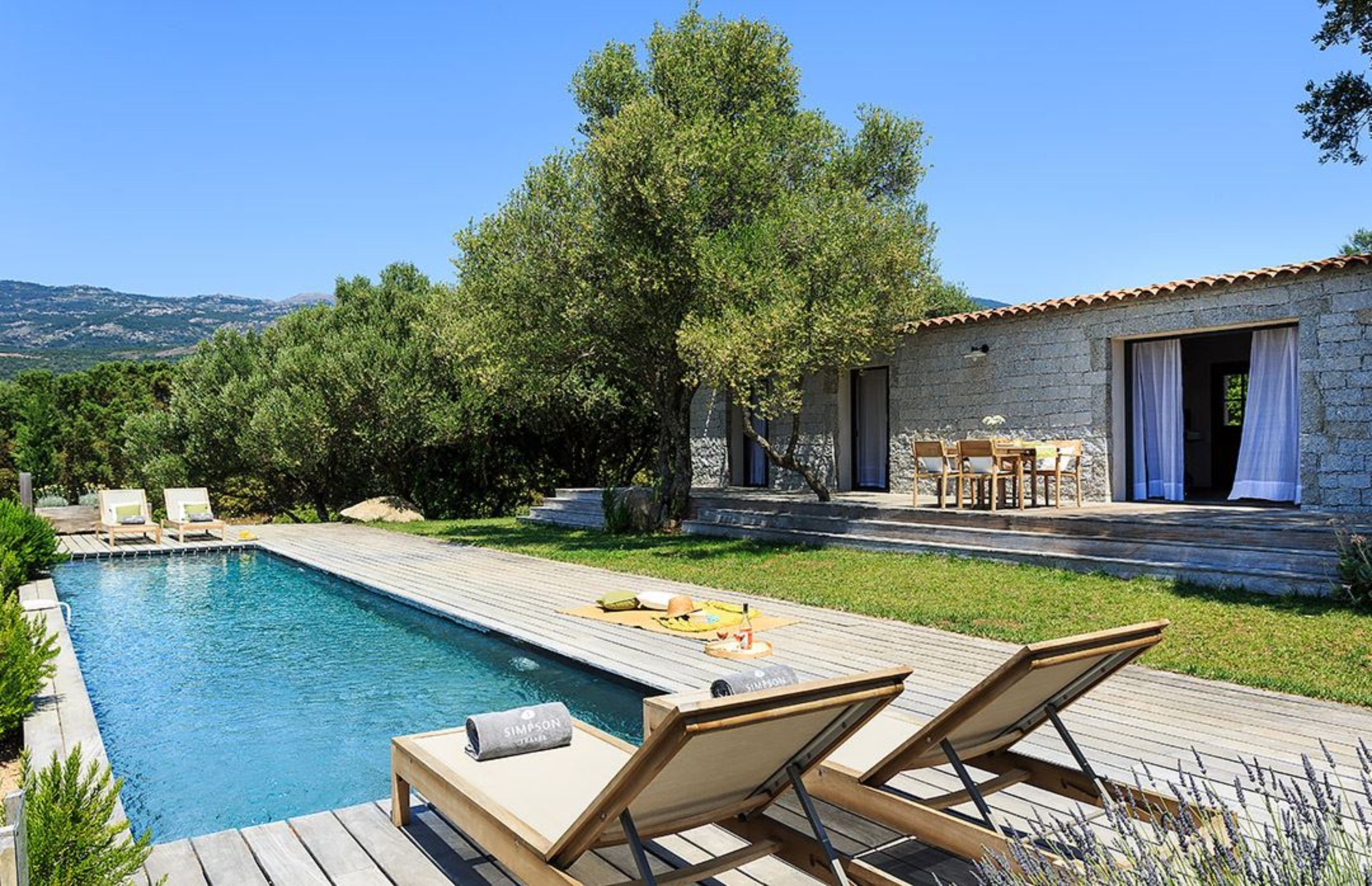 A poolside area with lounge chairs, a stone building, and a view of the surrounding landscape.