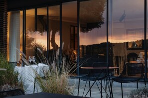 An outdoor dining area with tables and chairs, a view of the sunset, and a building with large windows.