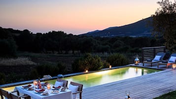 Un área de comedor al aire libre con piscina, terraza de madera y sillones de descanso.