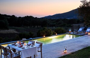 An outdoor dining area with a pool, wooden deck, and lounge chairs.