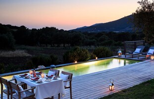 Un área de comedor al aire libre con piscina, terraza de madera y sillones de descanso.