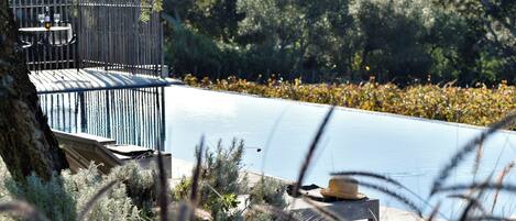 Un área junto a la piscina con una terraza de madera, una mesa con sillas y un sombrero sobre una mesita.