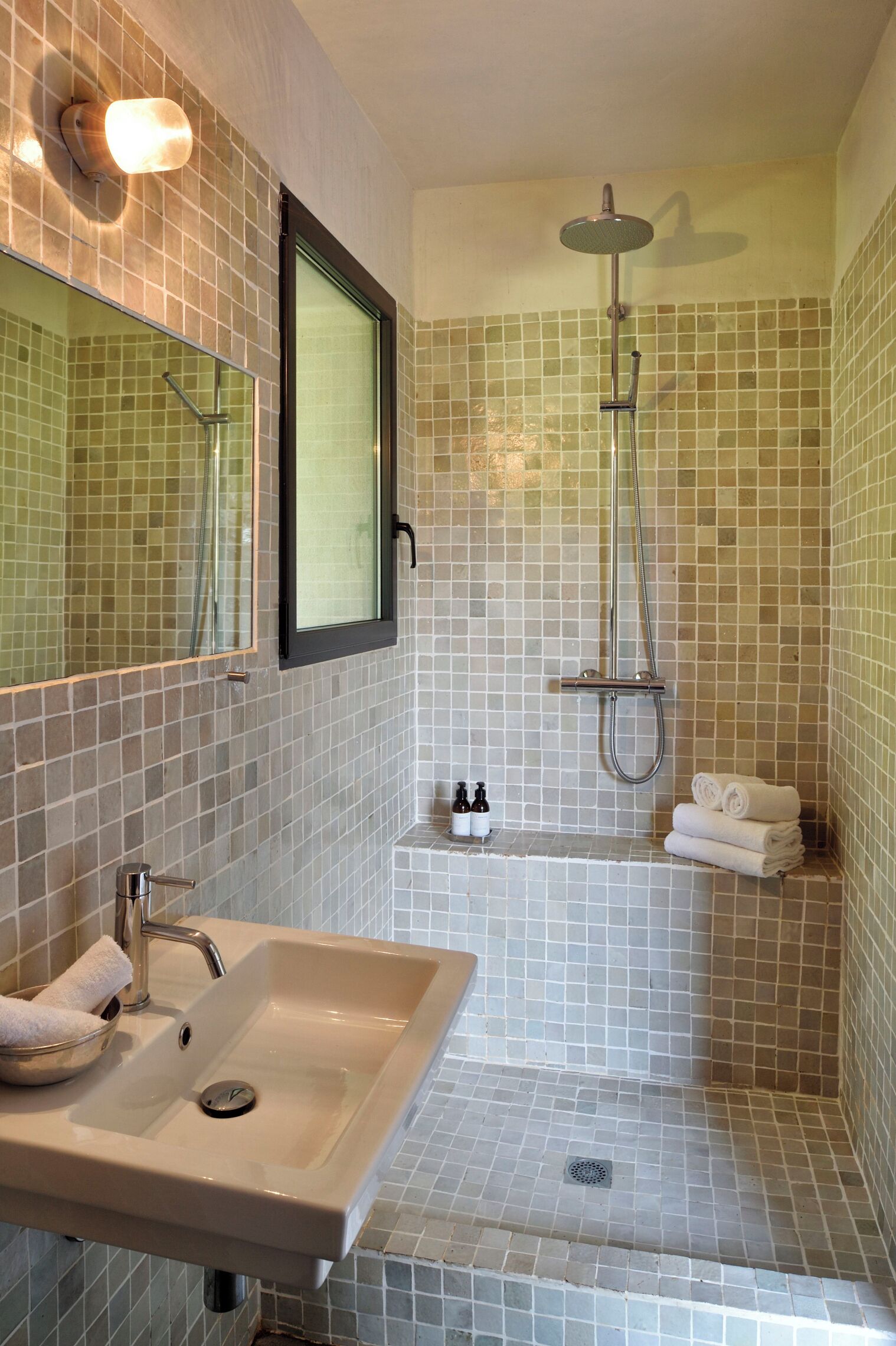 A bathroom with a sink, mirror, shower, and tiled walls.