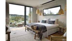 Quarto com cama grande, vista para o exterior e varanda com móveis de vime.