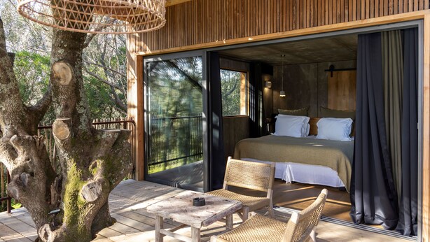 Um deck de madeira com uma cama, duas cadeiras de vime e uma mesa.