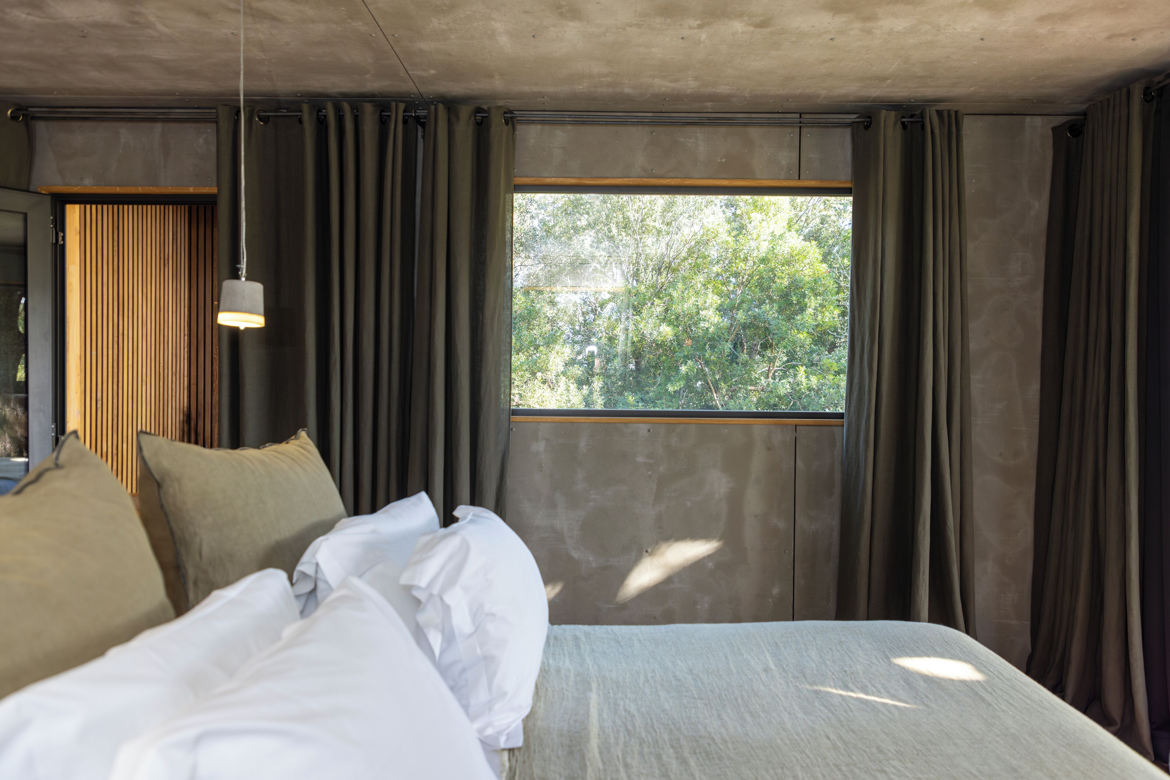 A bedroom with a large bed, a hanging light fixture, and a window with curtains.
