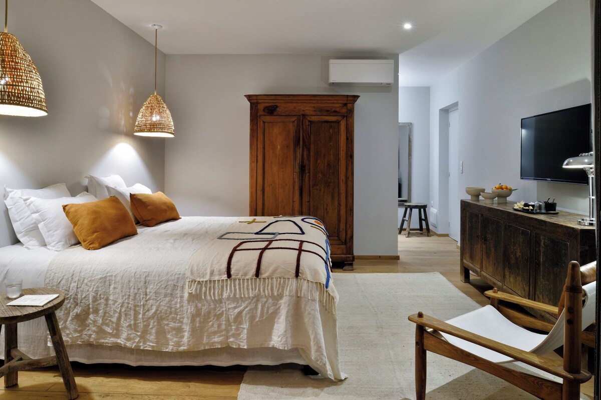 A bedroom with a bed, wooden wardrobe, TV, and a wooden chair.