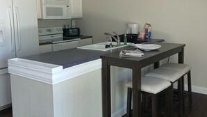 Una cocina moderna con una isla central, muebles blancos, microondas y cafetera.