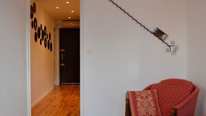 Un couloir doté d’un plancher en bois, d’un fauteuil rouge agrémenté de coussins à motifs et d’une décoration murale.