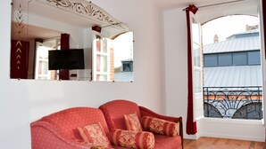 Un salon avec un canapé rouge, un grand miroir et une fenêtre donnant sur des immeubles.