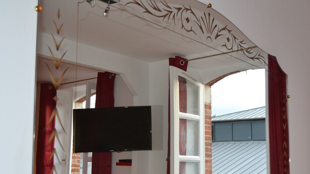 Une pièce avec un téléviseur fixé au mur, une fenêtre ornée de rideaux rouges et un plafond décoratif.
