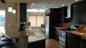A modern kitchen with dark cabinetry, a granite countertop, stainless steel appliances, and pendant lighting. - Hot Tub, Heated Pool and near Cape Coral, Punta Gorda Fort Myers & Naples  (North Fort Myers)