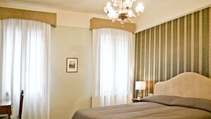 Une chambre d’hôtel avec un grand lit, une chaise, une table de chevet, une lampe et un lustre.