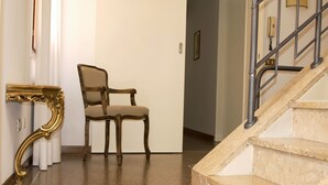 Un escalier avec des marches en marbre, une chaise et une console décorative dans un couloir.