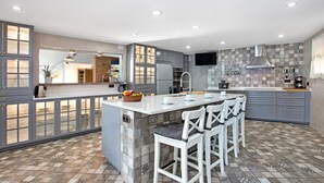 A modern kitchen with a central island, bar stools, and a tiled backsplash. - 2CANY01 - Spectacular luxury house with private outdoor and indoor pool, located in a privileged area on the cliff of Cala Canyelles with magnificent views of the sea (Lloret de Mar)