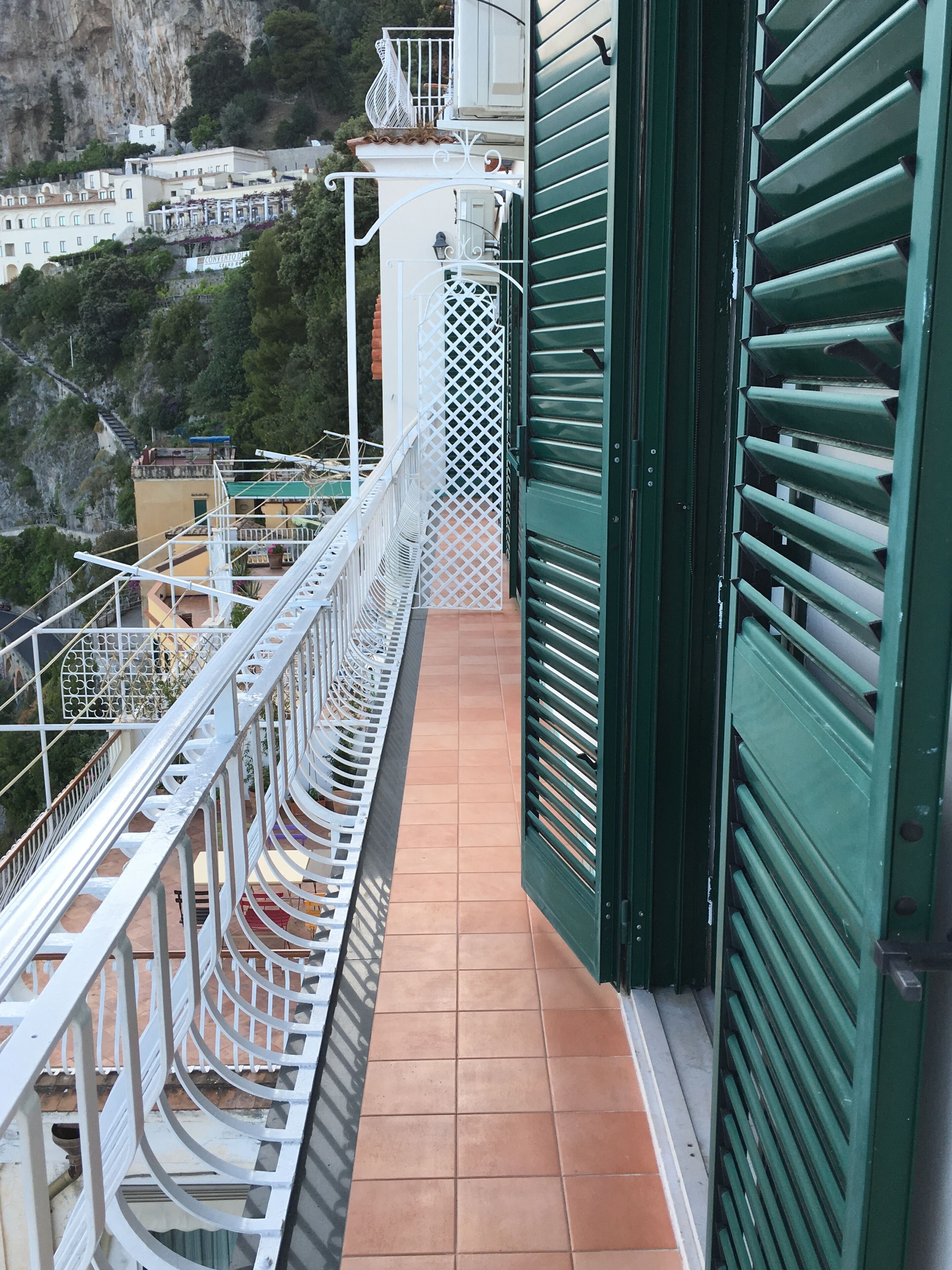 A balcony with a metal railing, a tiled floor, and a green shutter door.