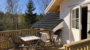 Een houten terras met een tafel, stoelen, een overdekt gedeelte en een deur naar binnen.