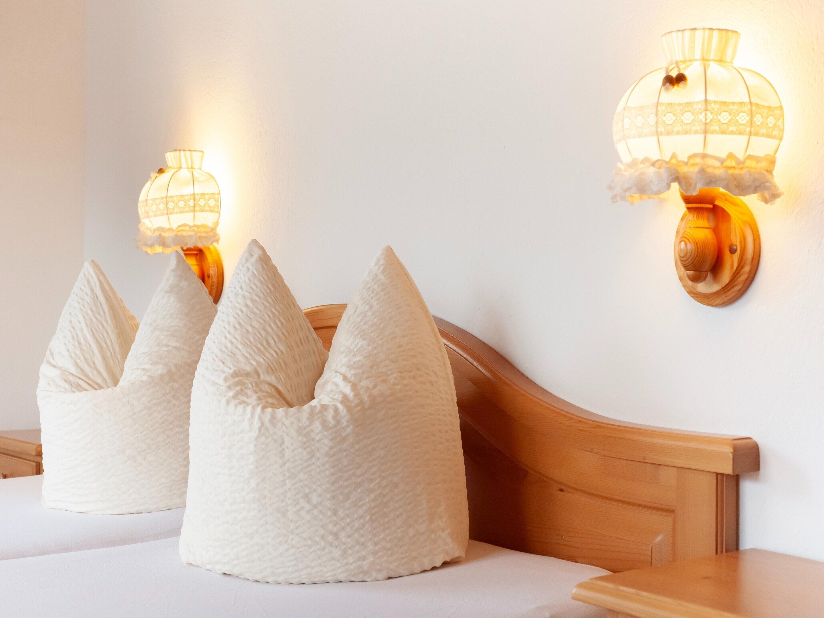 Une chambre à coucher avec une tête de lit en bois, trois oreillers blancs et deux lampes fixées au mur.