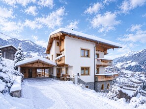 Un chalet à plusieurs étages, avec un toit enneigé, des balcons en bois et une vue imprenable sur les montagnes.