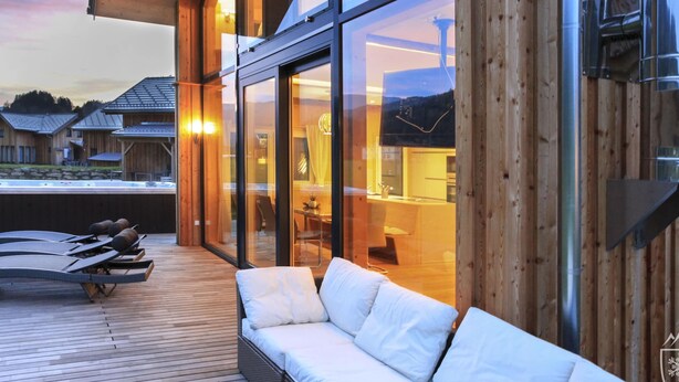 A modern outdoor seating area with a wooden deck and a white cushioned sofa. - Premium Chalet With Whirlpool (Murau)