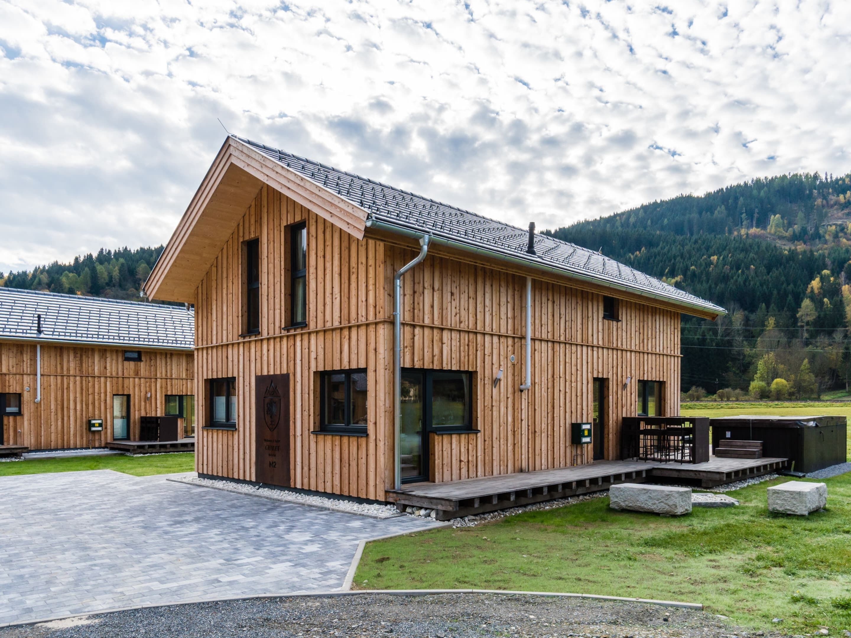 Eine Holzhütte mit geneigtem Dach, großen Fenstern und einer gepflasterten Auffahrt.