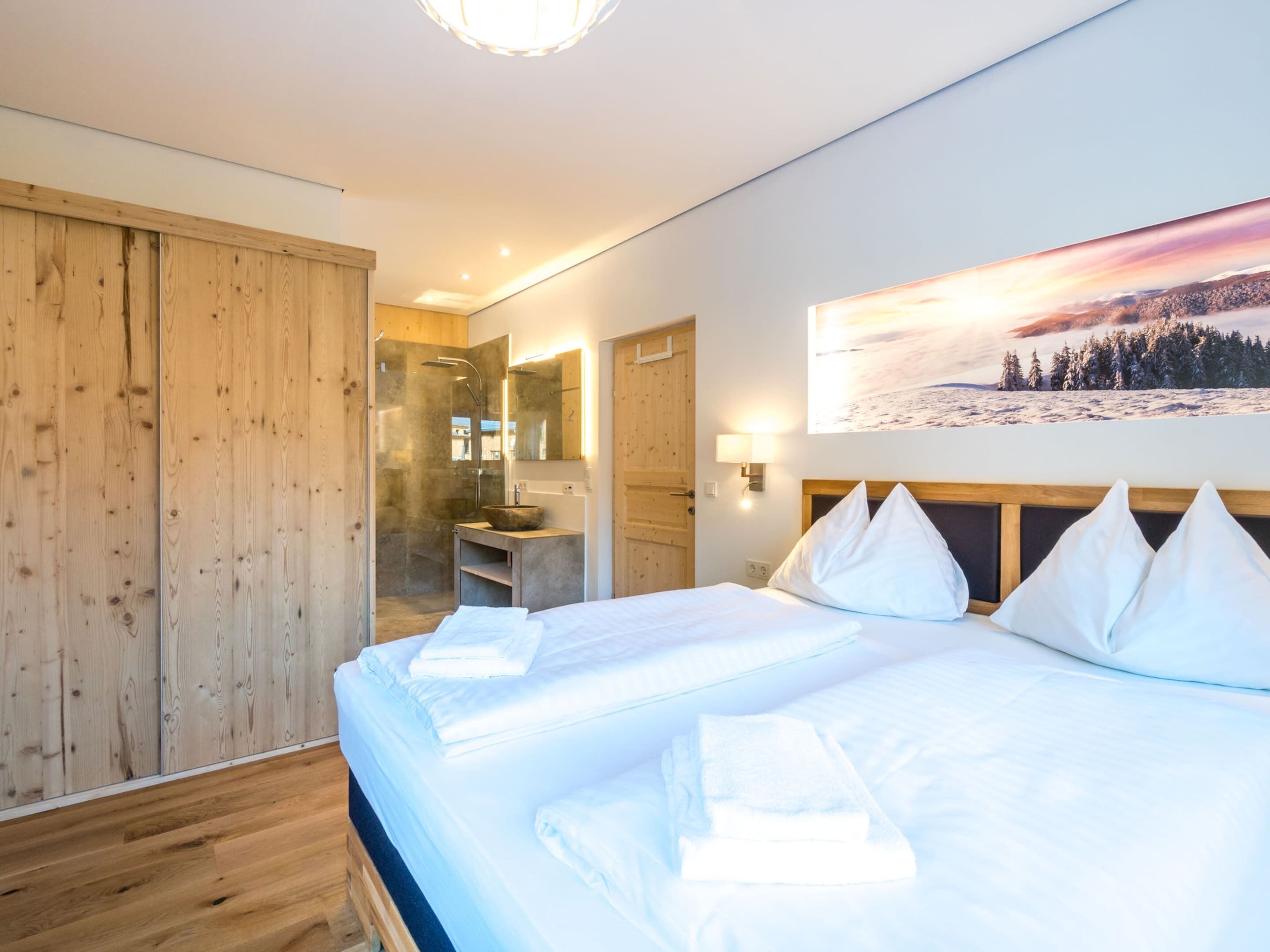 A modern hotel room with a large bed, wooden wardrobe, and a bathroom with a glass shower.