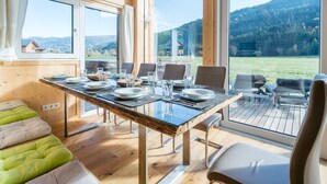 A dining area with a table set for four, large windows offering a view of a mountainous landscape. - Premium Chalet With Whirlpool (Murau)