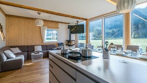 A modern kitchen with a central island, wooden beams, and large windows offering a view of the outdoors. - Premium Chalet With Whirlpool (Murau)