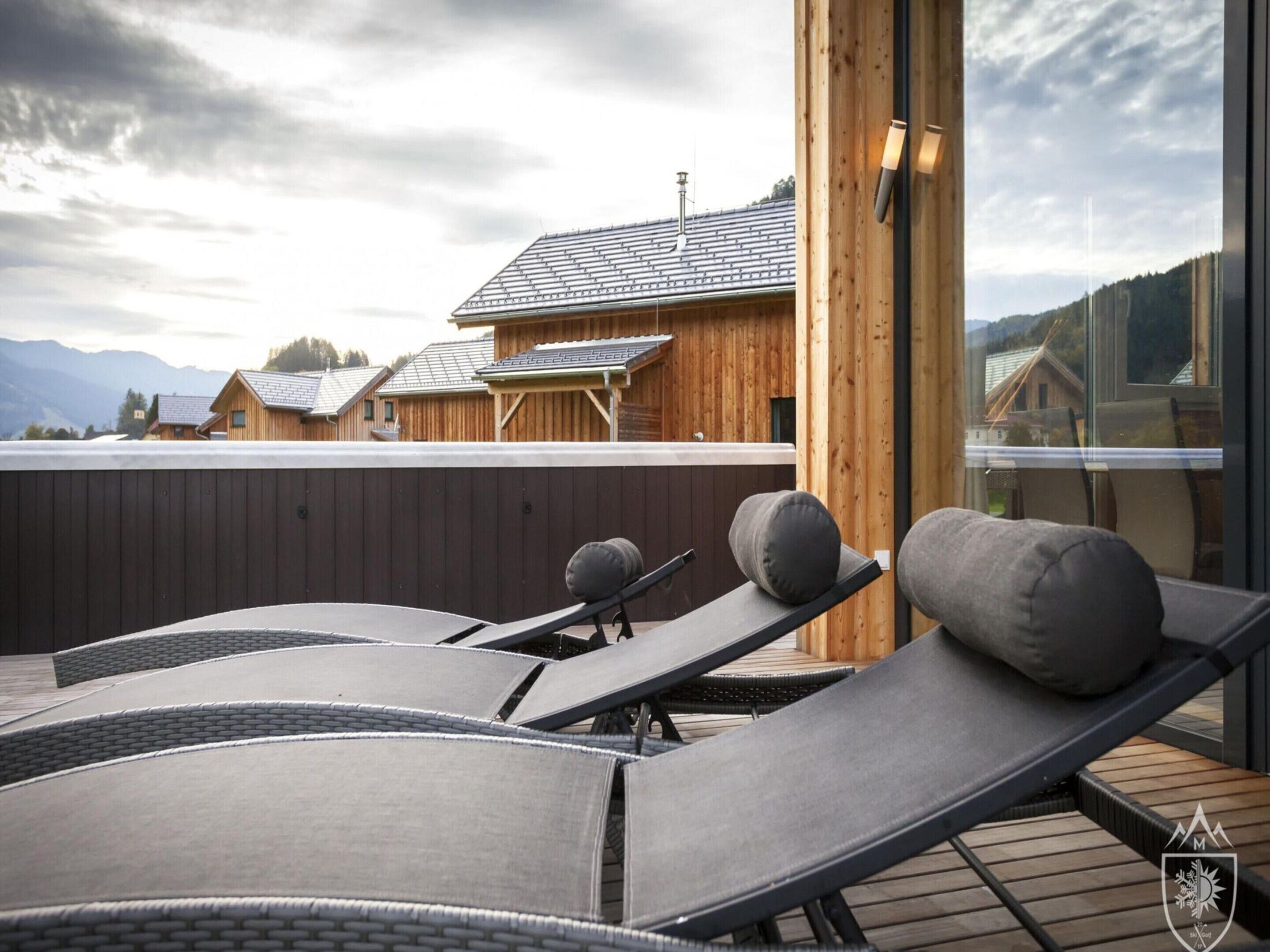 En takterrass med solstolar och ett trädäck, med utsikt över ett bergigt landskap och en rad trähus.