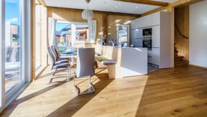 A modern kitchen with wooden beams, a dining area with a table and chairs, and a view of the outside. - Premium Chalet With Whirlpool (Murau)