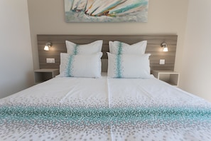 A double bed with a white and teal patterned bedspread, two white pillows with teal accents, wooden headboard, and two bedside tables with wall-mounted lamps. - Luxury Villa With Private Pool in Cesseras (Cesseras)