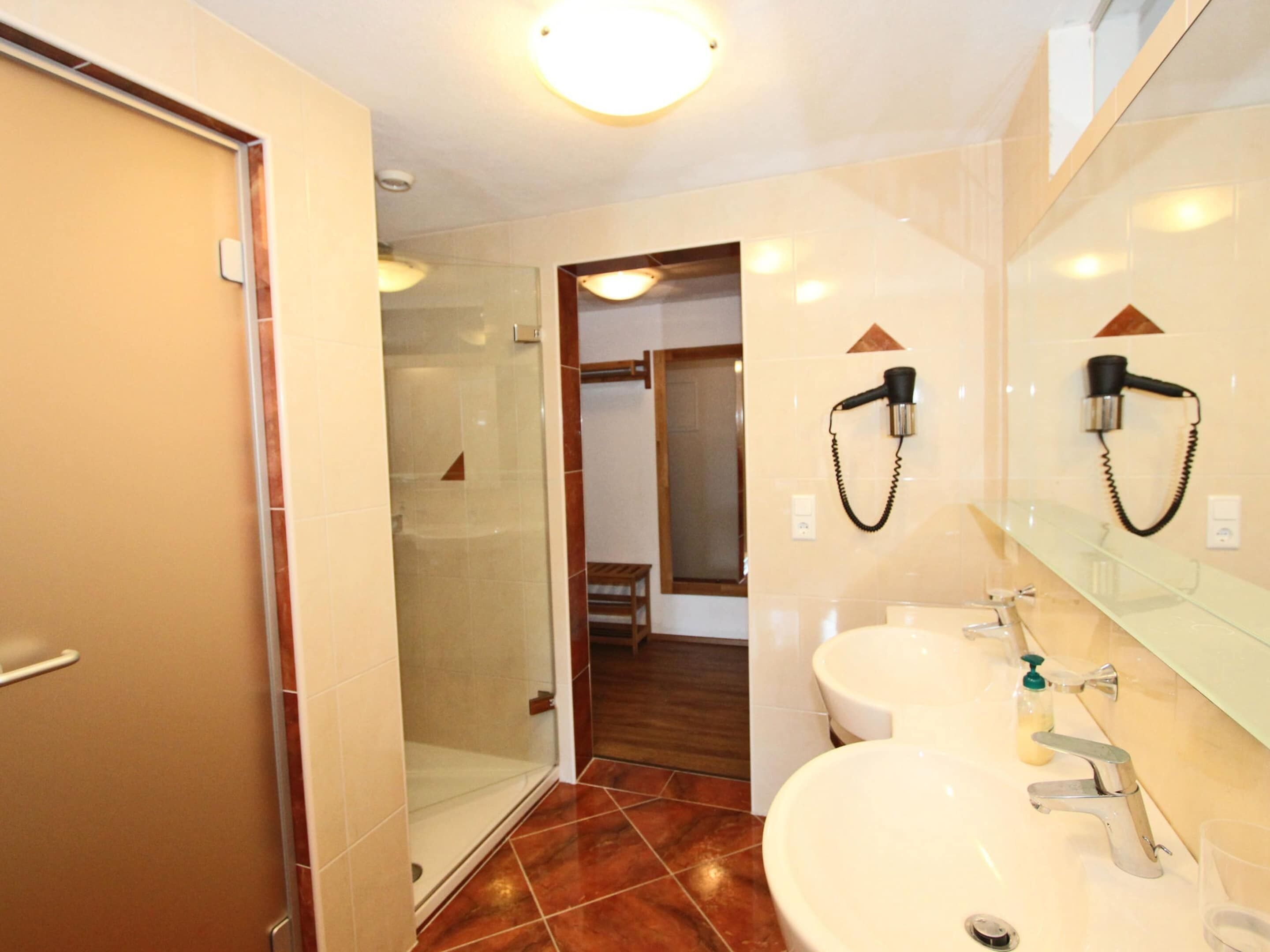 Une salle de bain avec deux lavabos, une douche à parois de verre et un sèche-cheveux fixé au mur.