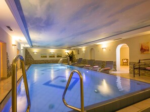 En pool med ett stjärnmönstrat tak, solstolar och en vägg av sten.