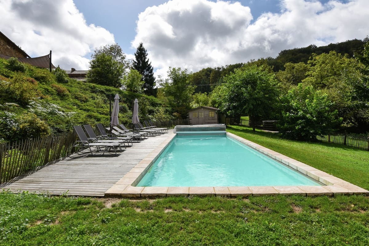A rectangular swimming pool with a wooden deck and lounge chairs on one side.