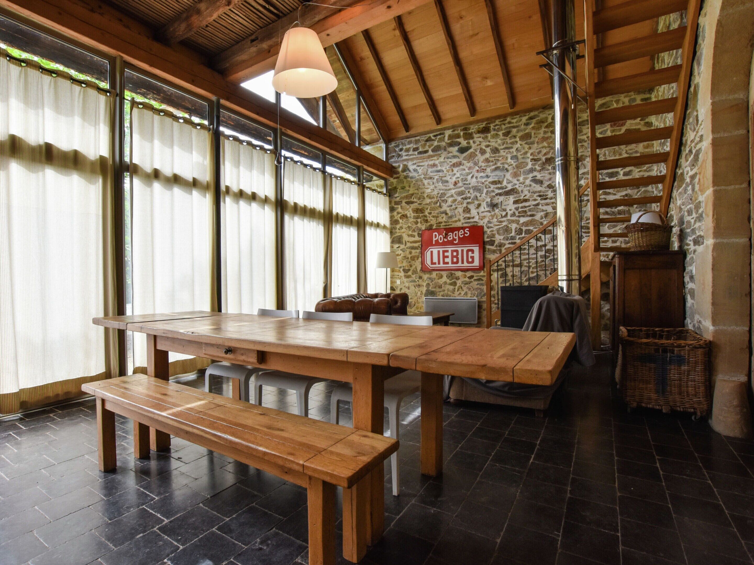 Un intérieur rustique avec une table en bois, des bancs, des murs en pierre et un escalier.
