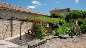 A stone building with a tiled roof, a wooden bench, and a garden with various plants and rocks. - Courry Gem: Pool & Charm (Courry)