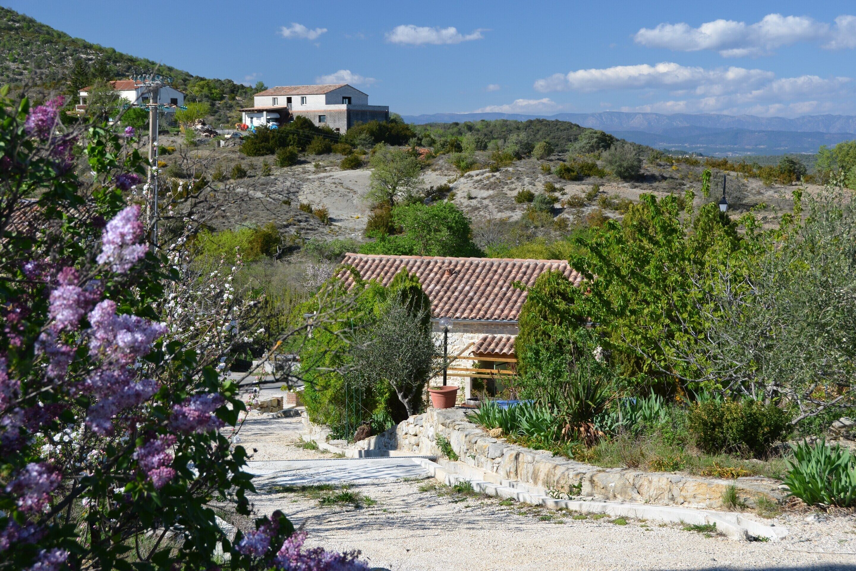 A rural landscape with a house on a hill, surrounded by vegetation and a clear sky.